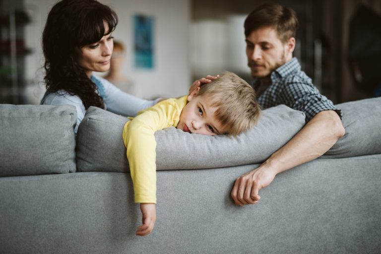 Little boy with Reactive Attachment Disorder (RAD) hanging arm over back of couch between parents