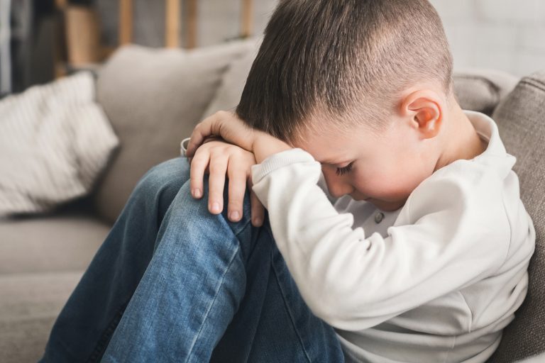child with depression hugging his knees while sitting on sofa