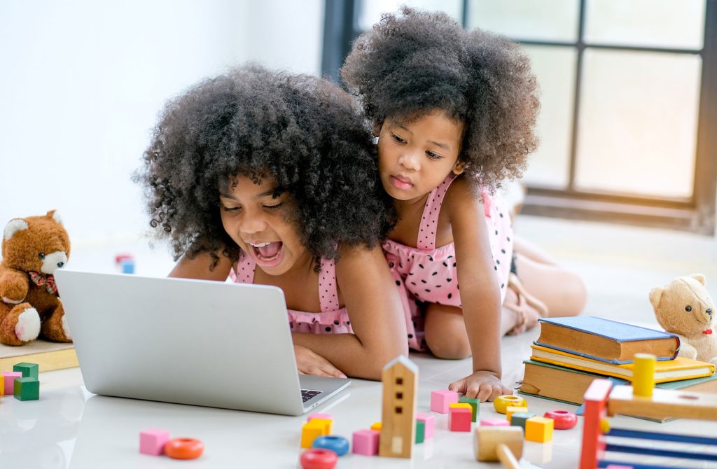 two little black girls playing with laptop in playroom